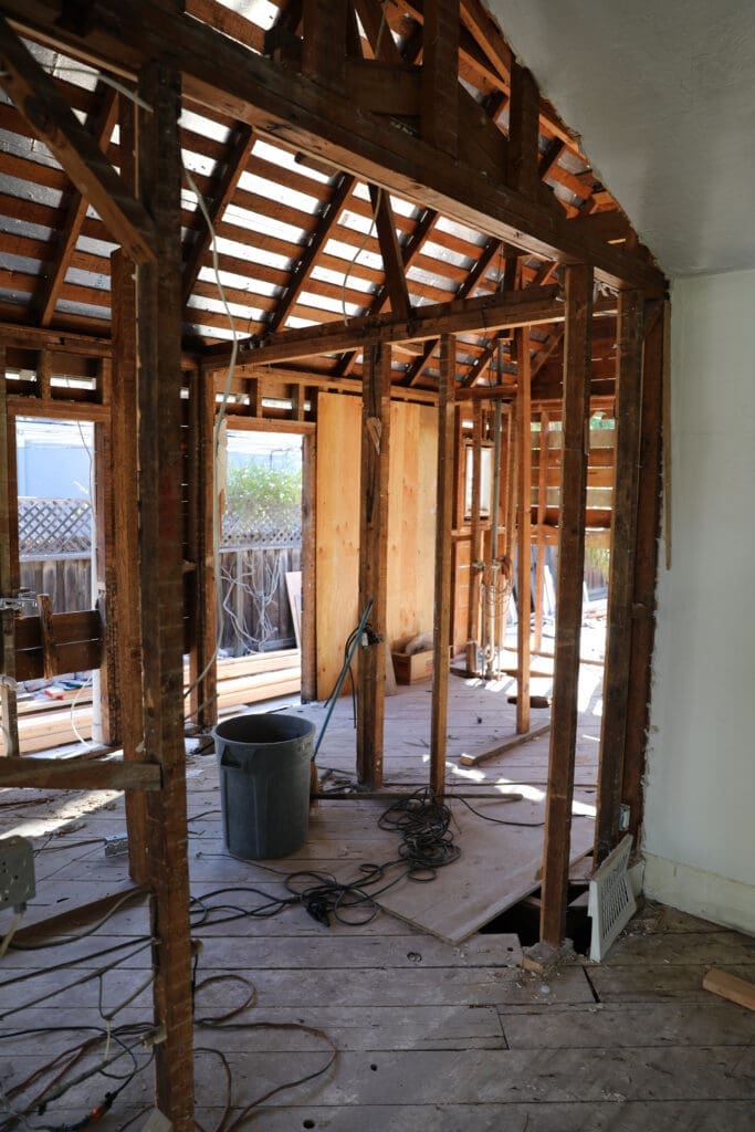 Interior of Willow Glen home during renovation showing exposed framing and temporary wooden floor after removing damaged original flooring.